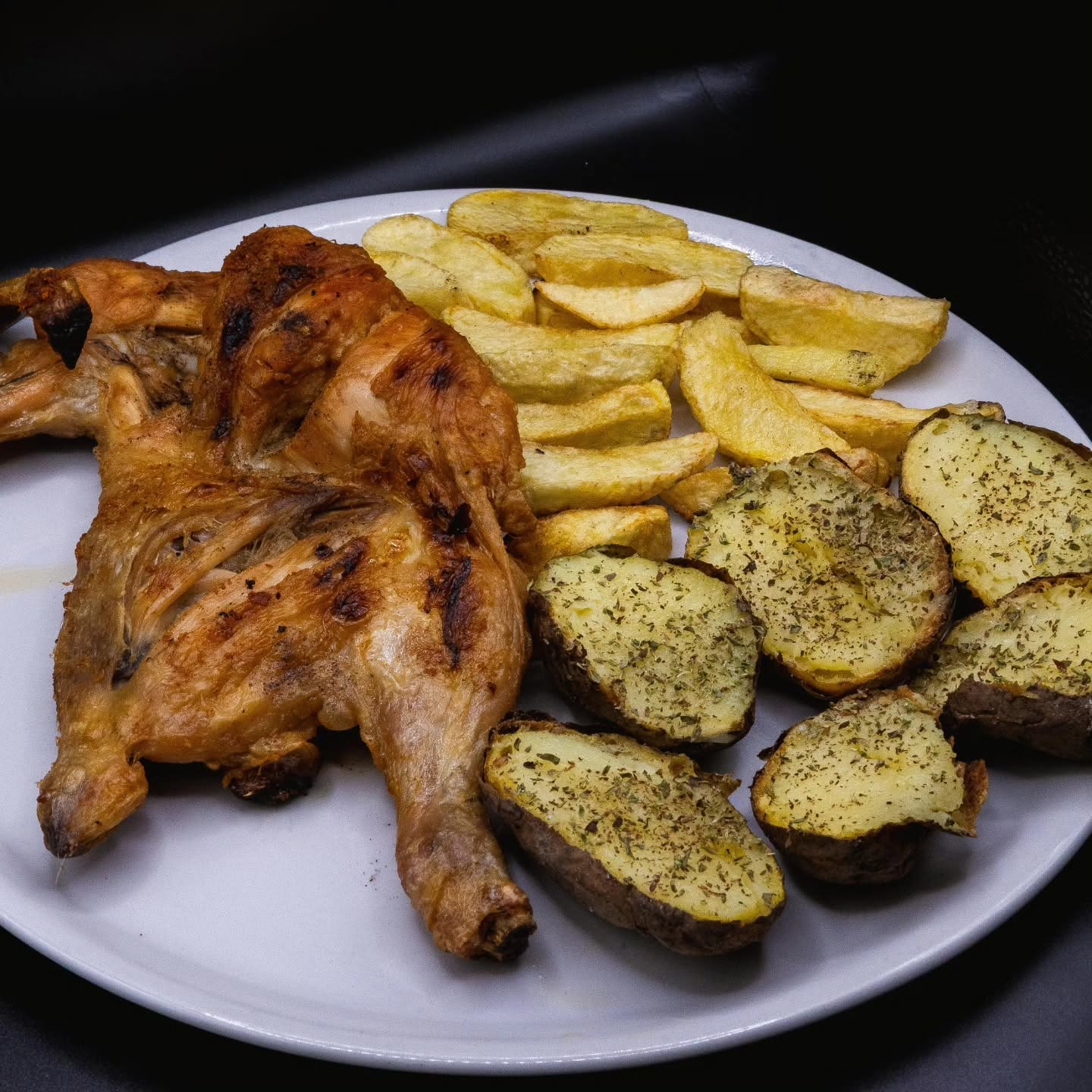 Pollo alla Kociss arrosto con patate fritte a spicchi e patate al forno alle erbe su piatto bianco, sfondo scuro